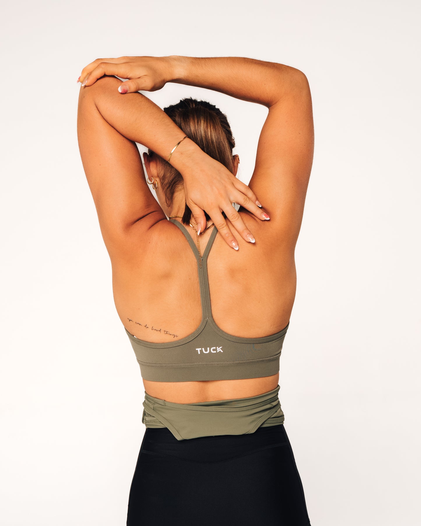 Person wearing a green sports bra with 'TUCK' branding on a white background