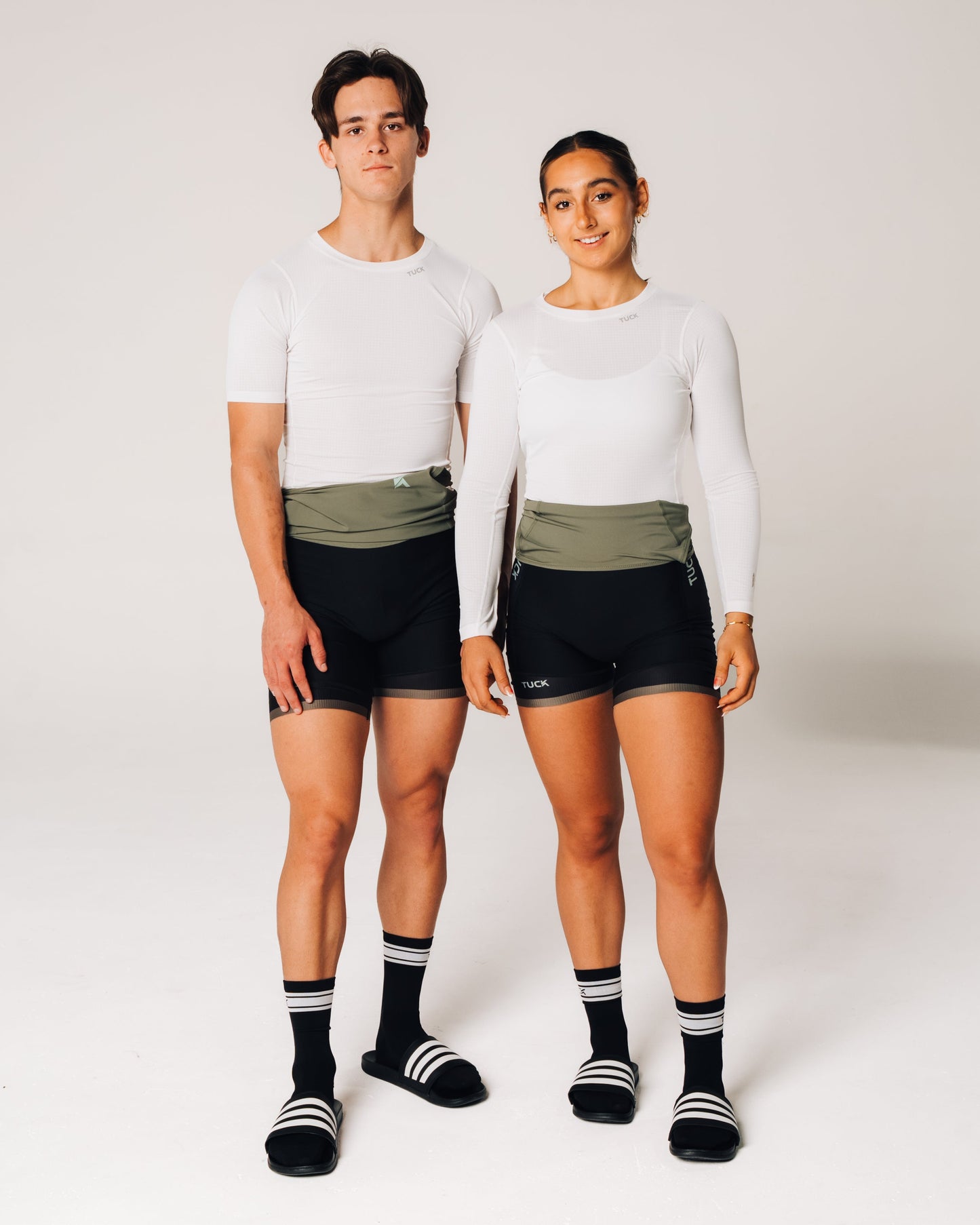 Two people wearing matching athletic outfits with shorts and socks on a plain background