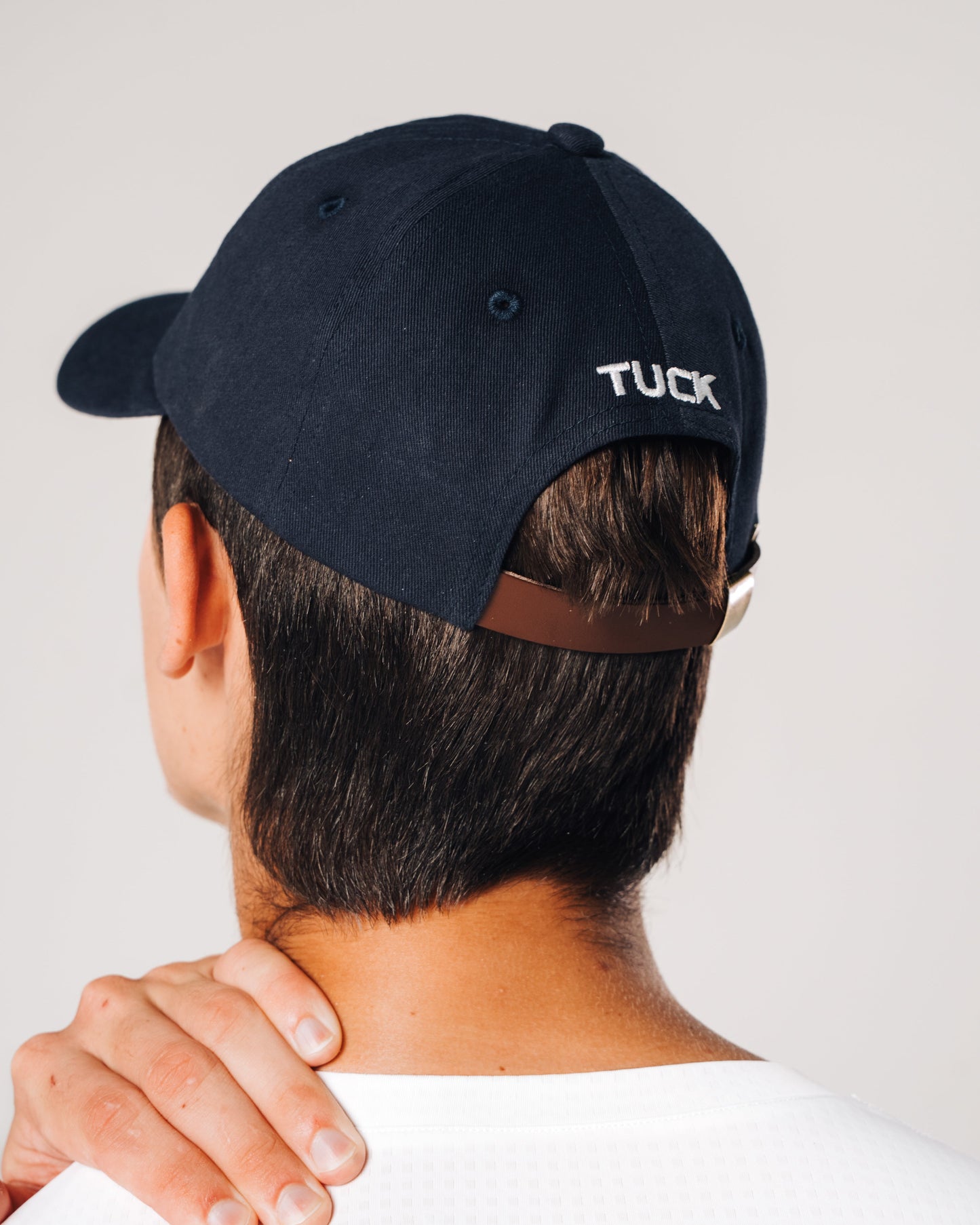 Person wearing a navy blue cap with 'TUCK' branding on the back, against a plain background.