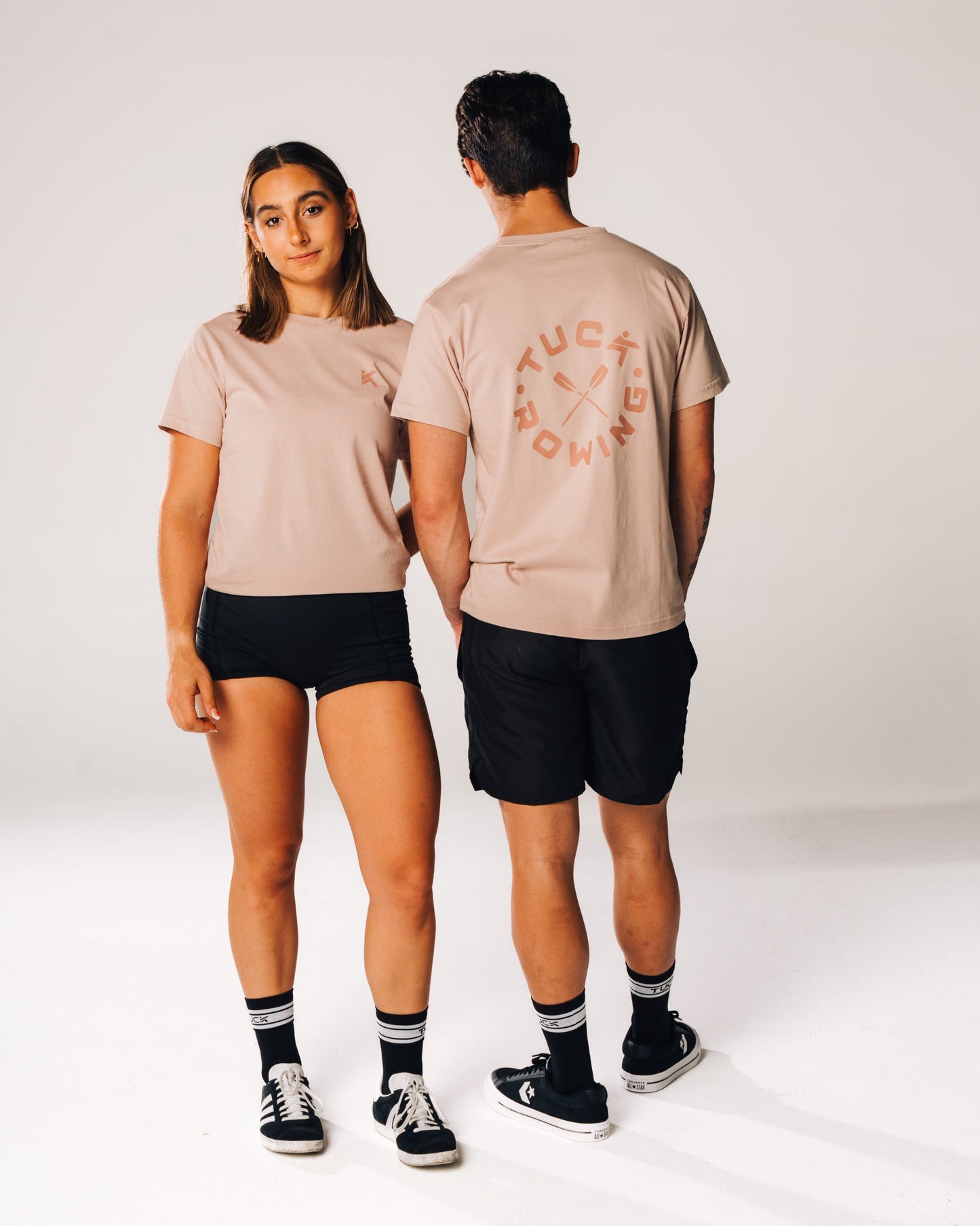 Two people wearing matching beige t-shirts with a logo on a white background