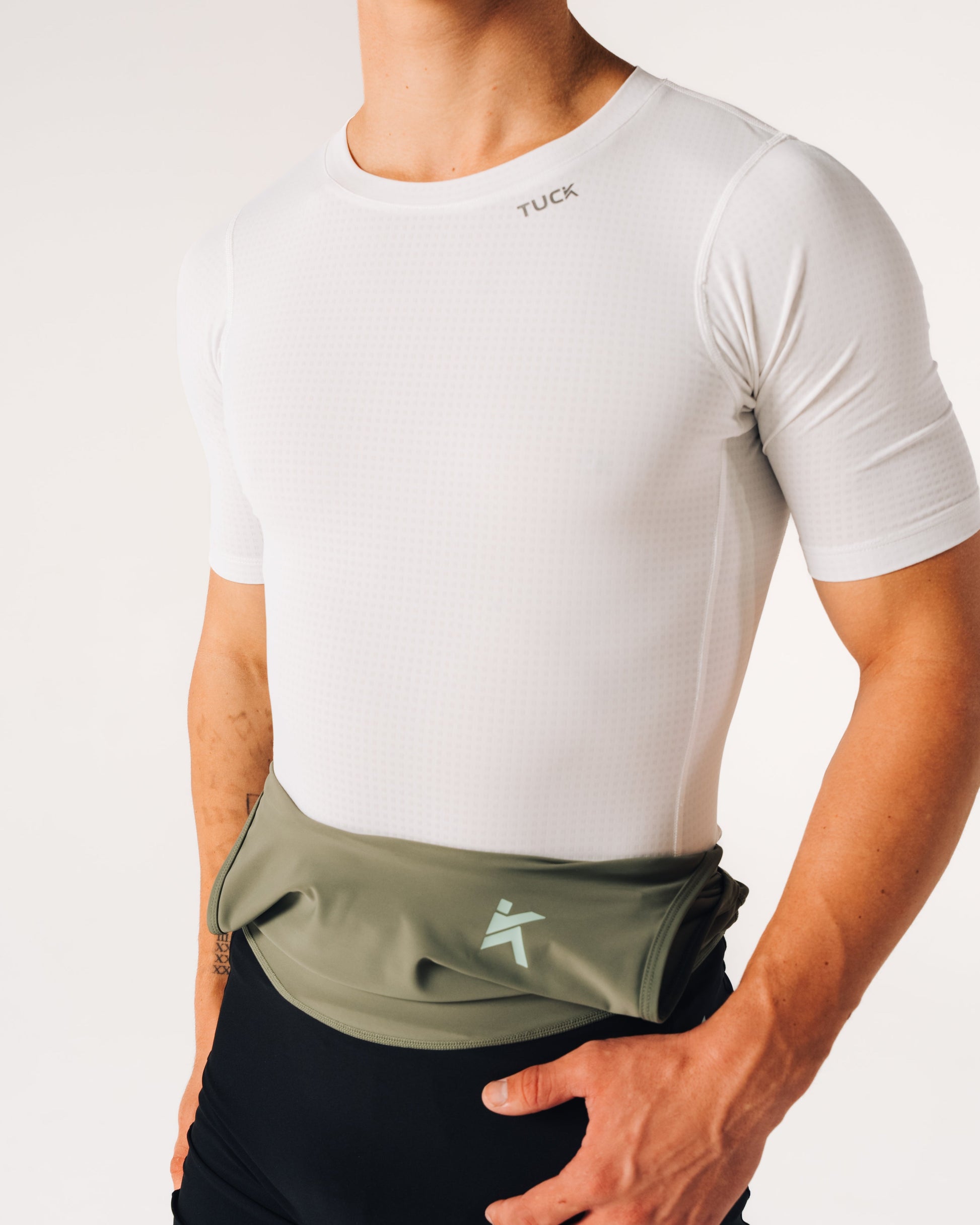 Person wearing a white t-shirt and green waist bag with a logo on a light gray background