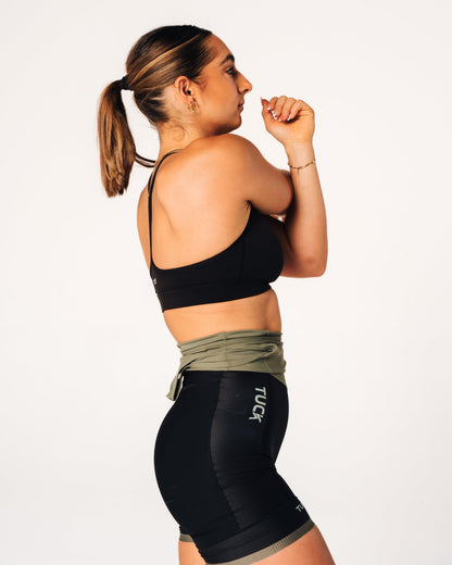Woman wearing a black sports bra and black leggings with visible branding on a white background
