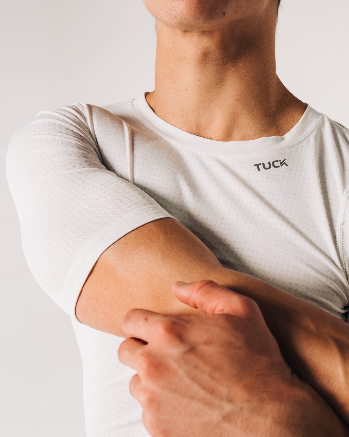 Person wearing a white t-shirt with 'TUCK' branding, holding their arm.