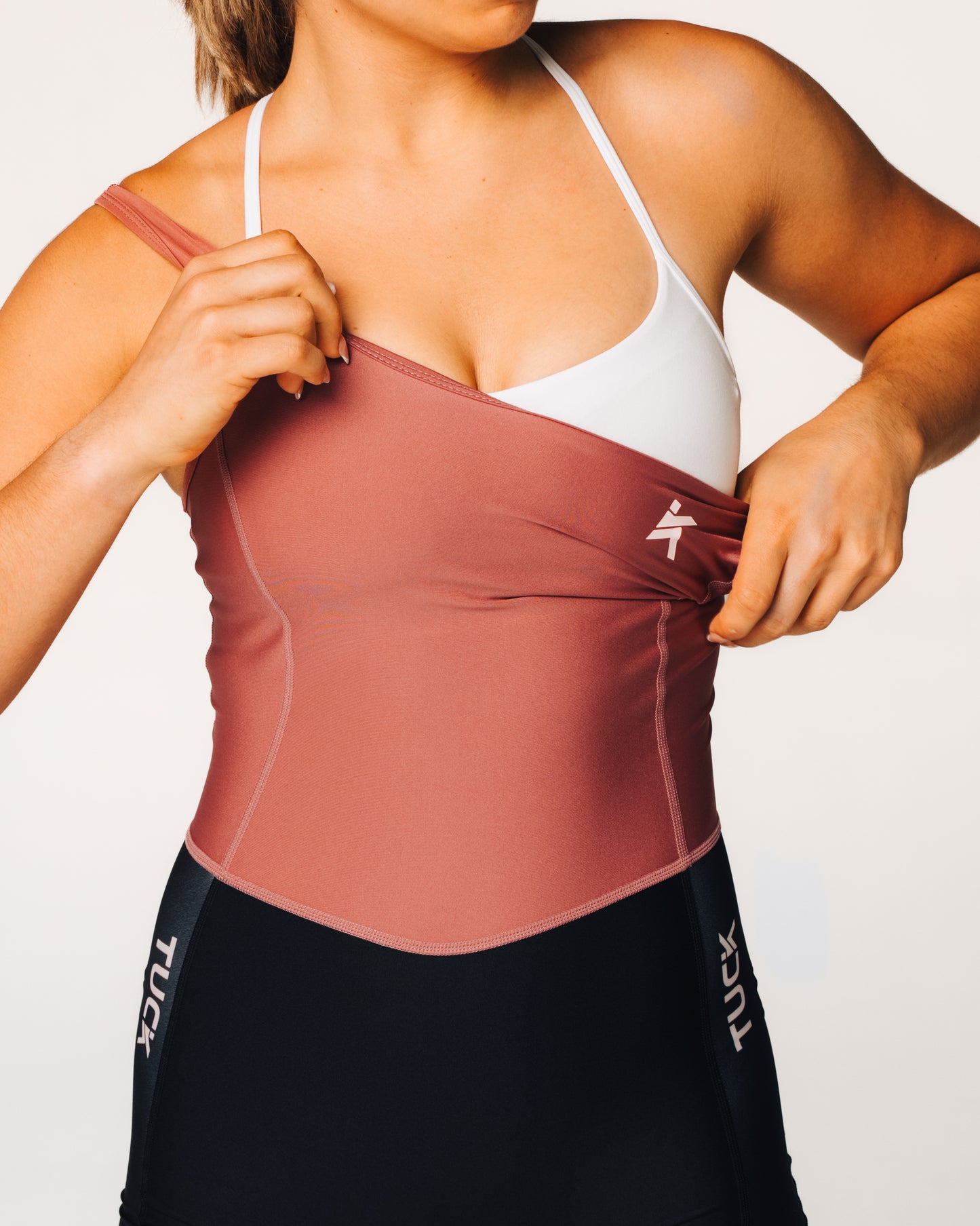 Person wearing a maroon athletic top with a white sports bra underneath, on a plain background.
