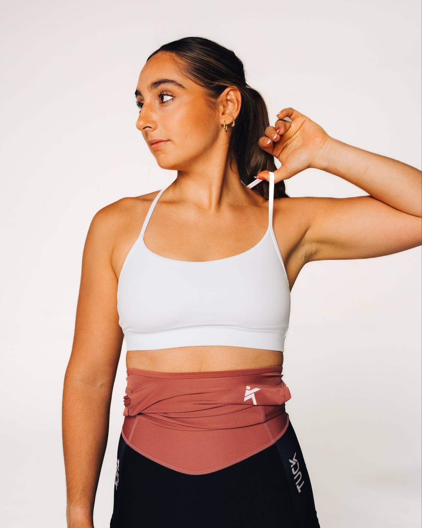 Woman wearing a white sports bra and black leggings with a visible brand logo on a plain background
