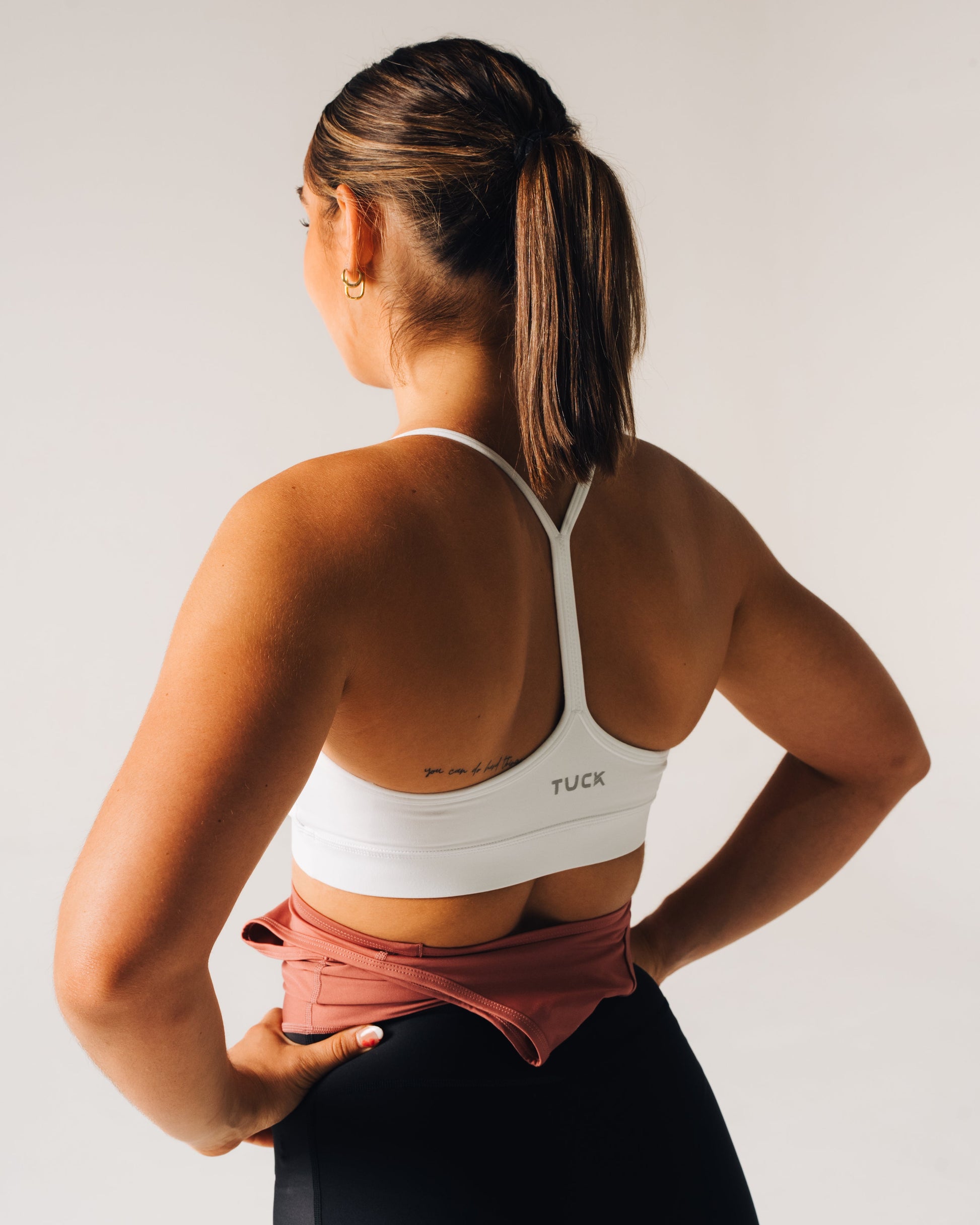 Woman wearing a white sports bra with 'TUCK' branding, standing against a plain background.