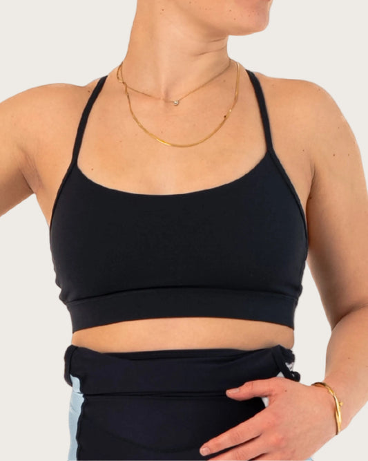 Woman wearing a black sports bra and black cycling shorts with light blue accents on a white background